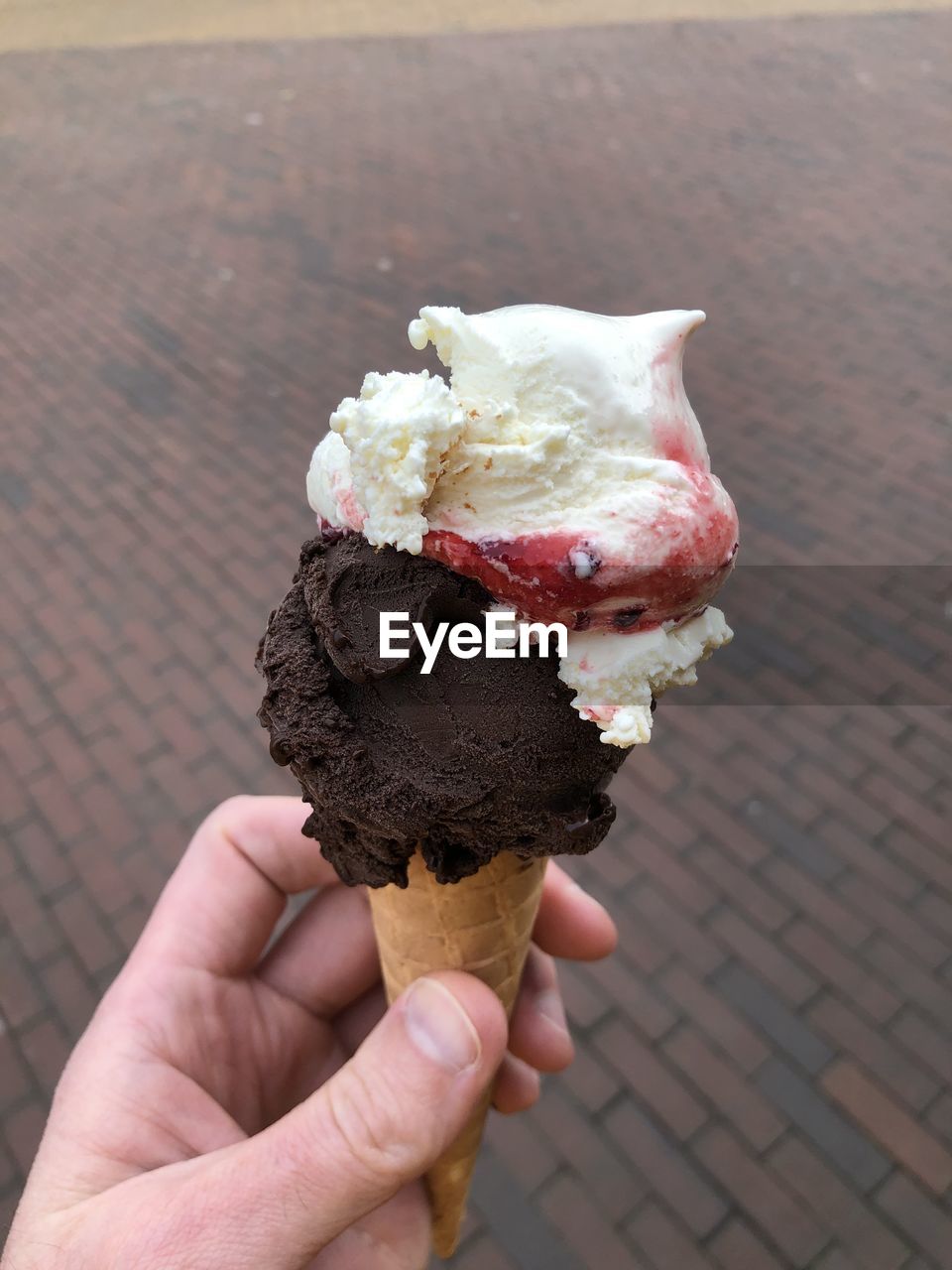 CROPPED HAND HOLDING ICE CREAM CONE ON ROCK