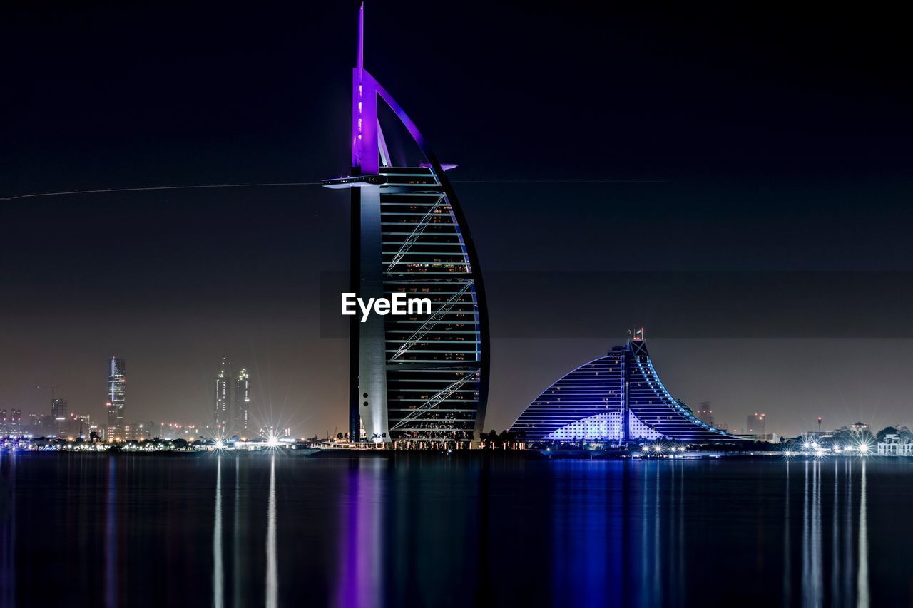 Illuminated burj al arab hotel by sea against sky in city at night