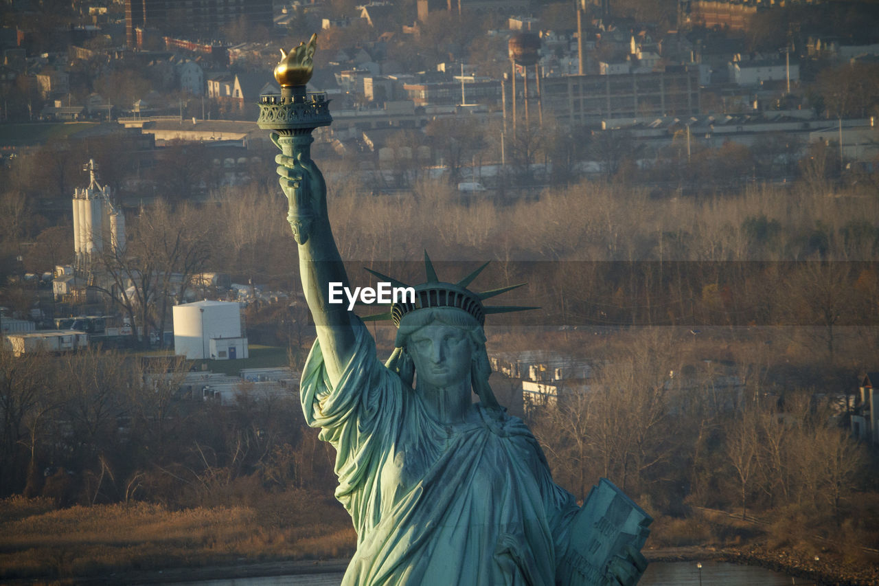 The statue of liberty in front of new jersey industrial suburbs, nyc.