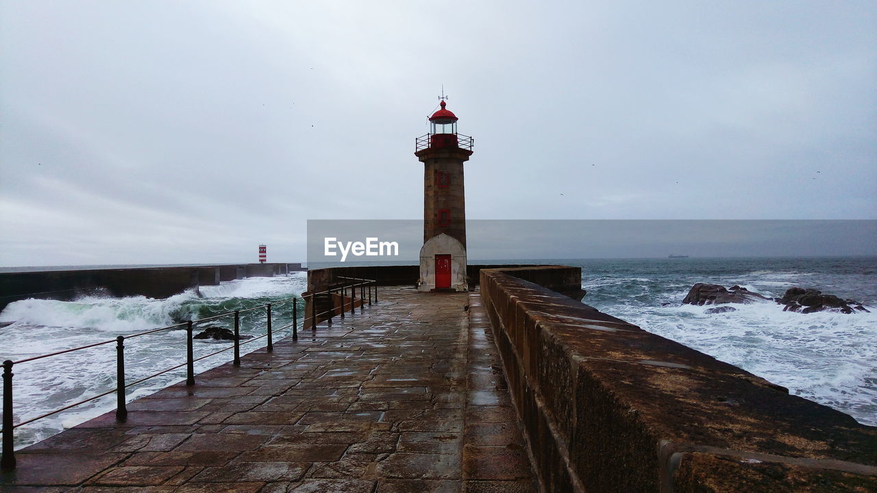 Lighthouse amidst sea and buildings against sky