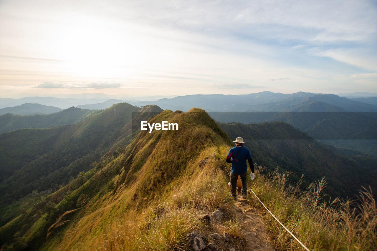 FULL LENGTH REAR VIEW OF MAN ON MOUNTAIN AGAINST SKY