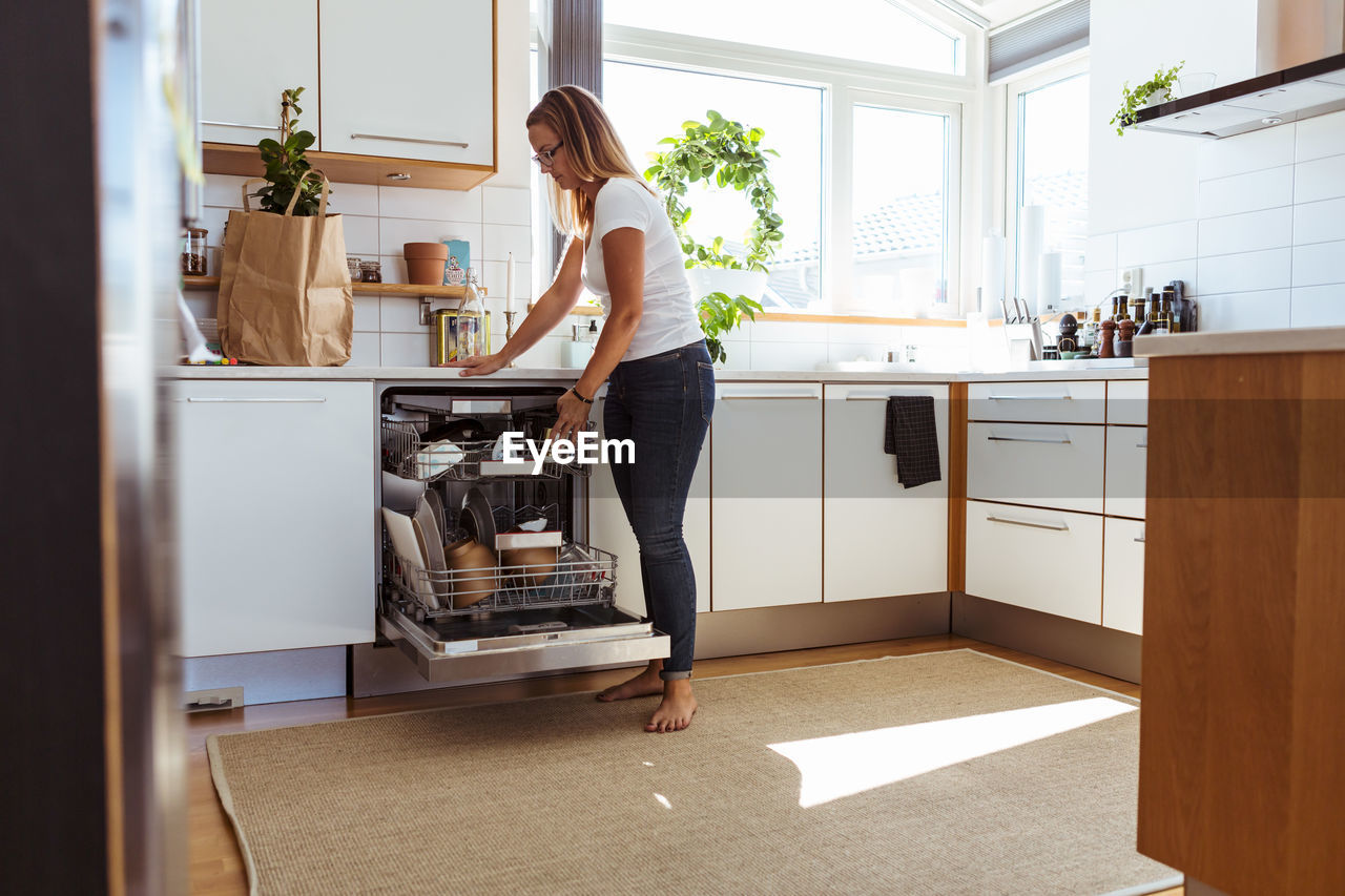 Full length of woman using dishwasher while standing in kitchen