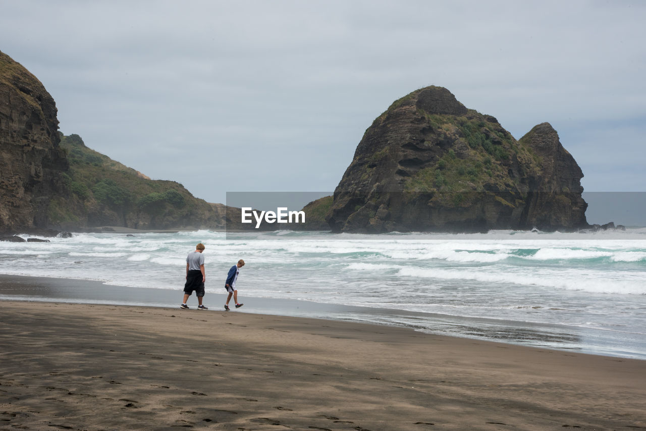 Siblings walking at beach against sky