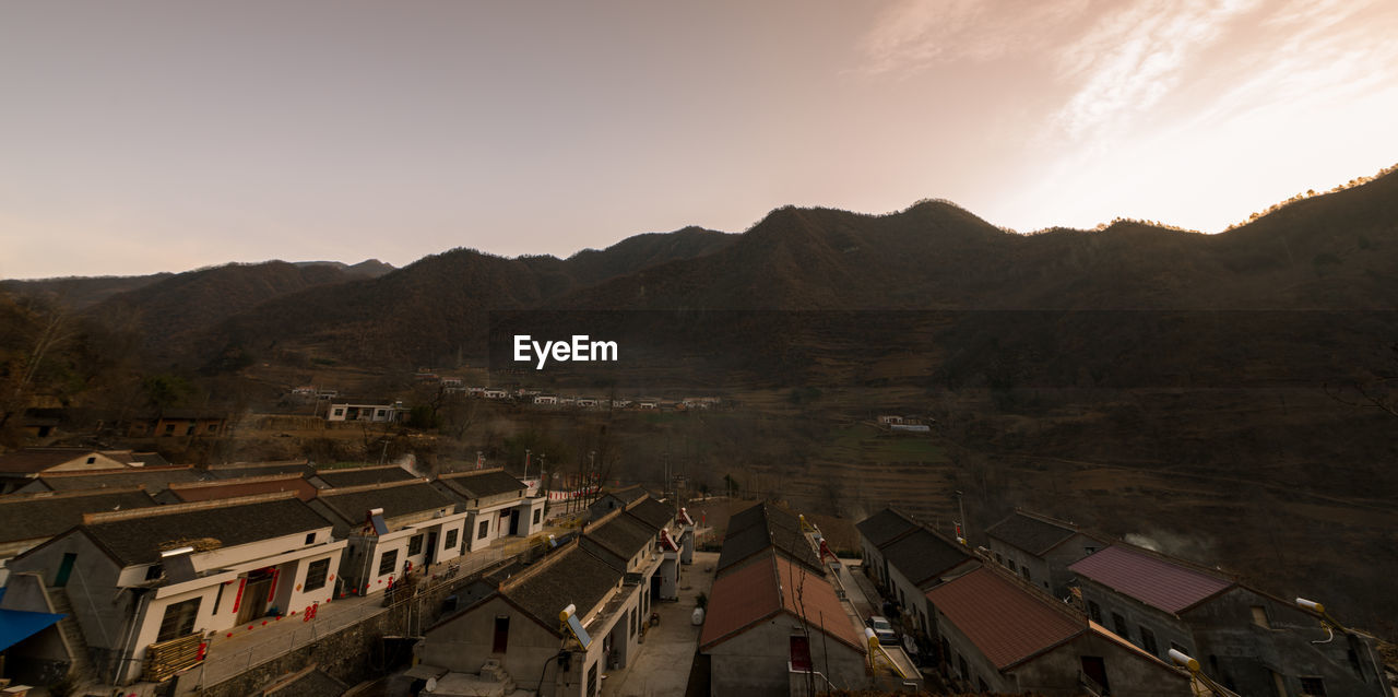 HIGH ANGLE VIEW OF TOWNSCAPE BY MOUNTAINS AGAINST SKY