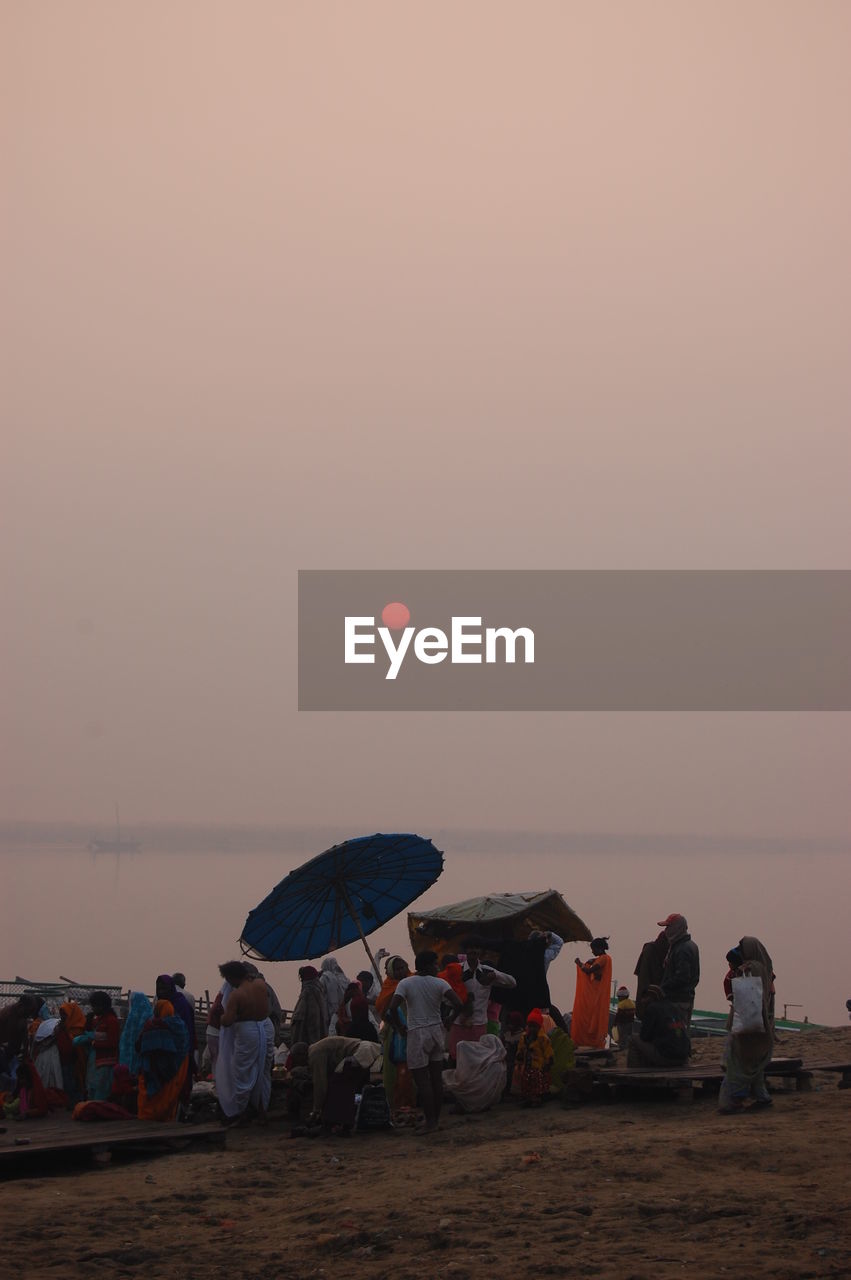 People standing at beach against sky during sunrise