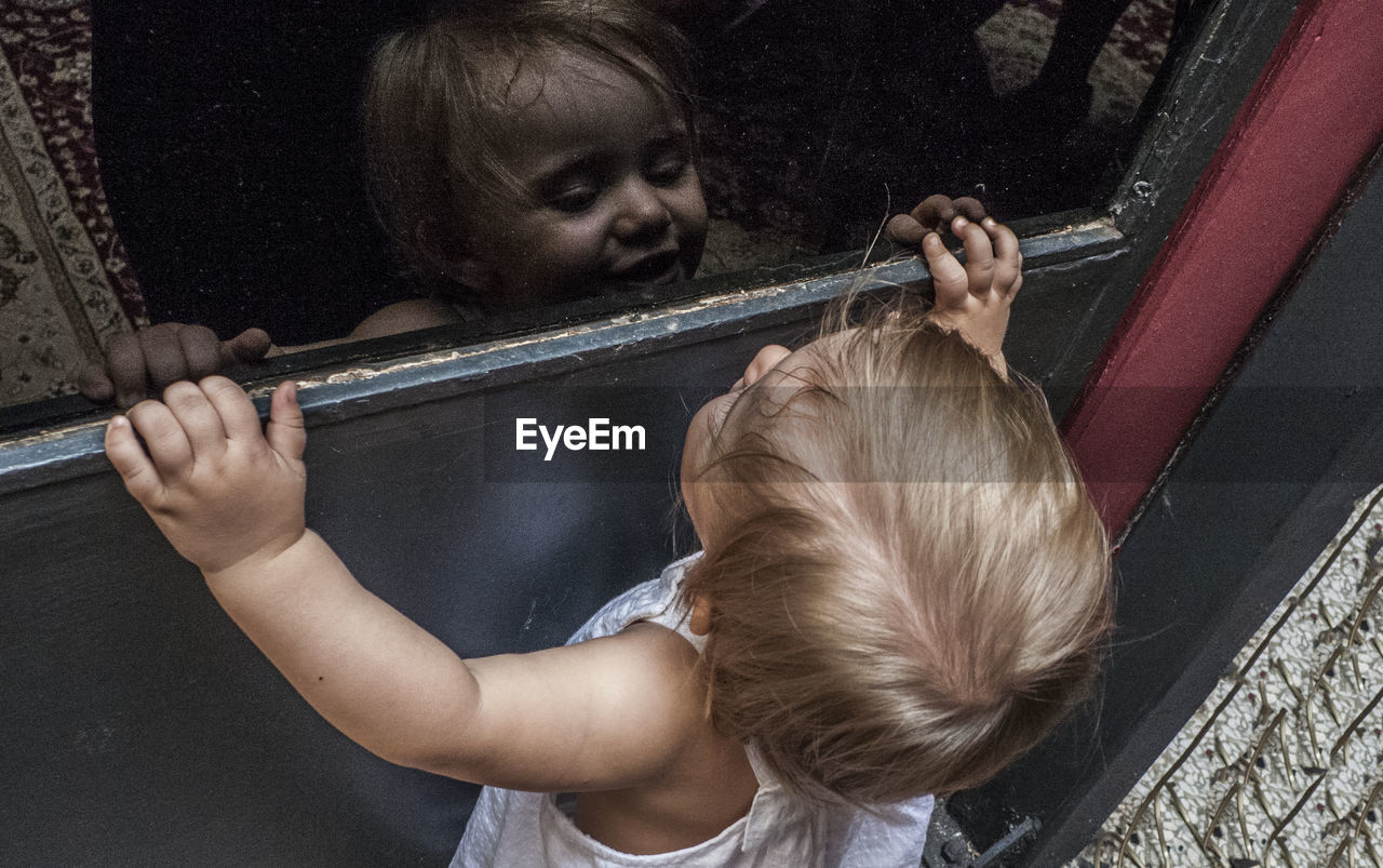 High angle view of cute girl looking at her own reflection on glass window