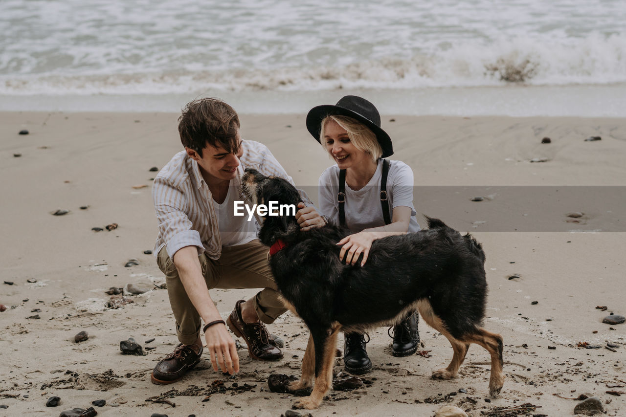 Young attractive couple having fun at he beach with a dog