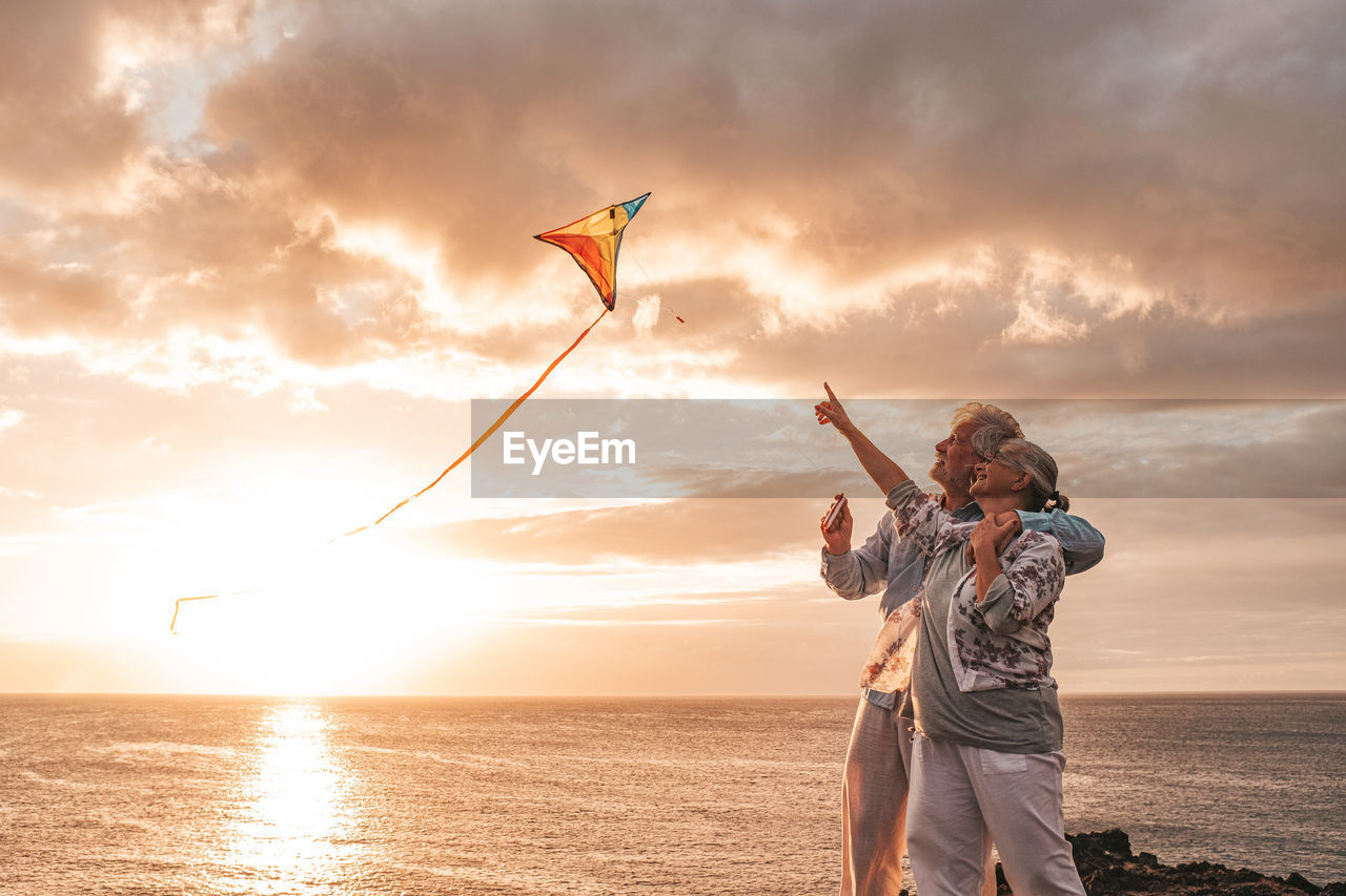 Senior couple flying kite while standing at beach against sky