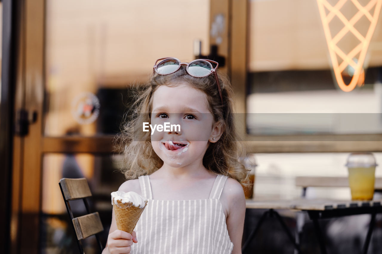 Toddler child eating cone ice cream outside near cafe. cute blonde caucasian girl licking frozen