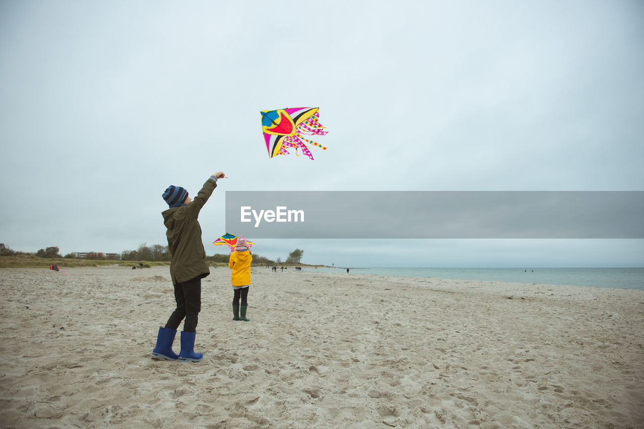 Rear view of boy holding kite standing on beach against sky