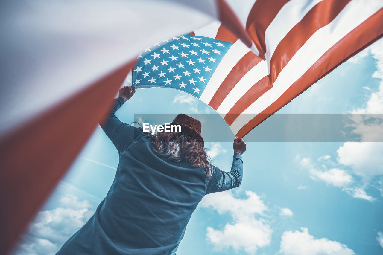 LOW ANGLE VIEW OF WOMAN HOLDING FLAG AGAINST SKY