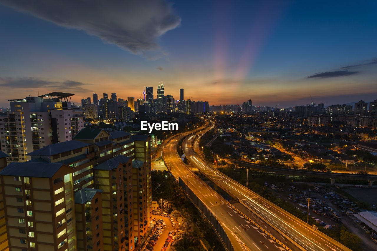 HIGH ANGLE VIEW OF ILLUMINATED STREET AMIDST BUILDINGS IN CITY