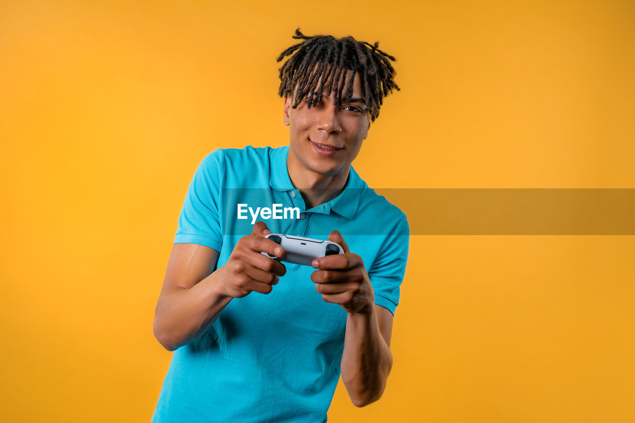 one person, colored background, technology, holding, adult, studio shot, men, wireless technology, smartphone, portable information device, waist up, yellow, mobile phone, indoors, smiling, person, portrait, orange color, blue, yellow background, copy space, young adult, front view, communication, lifestyles, activity, casual clothing, standing, happiness, emotion, clothing, looking