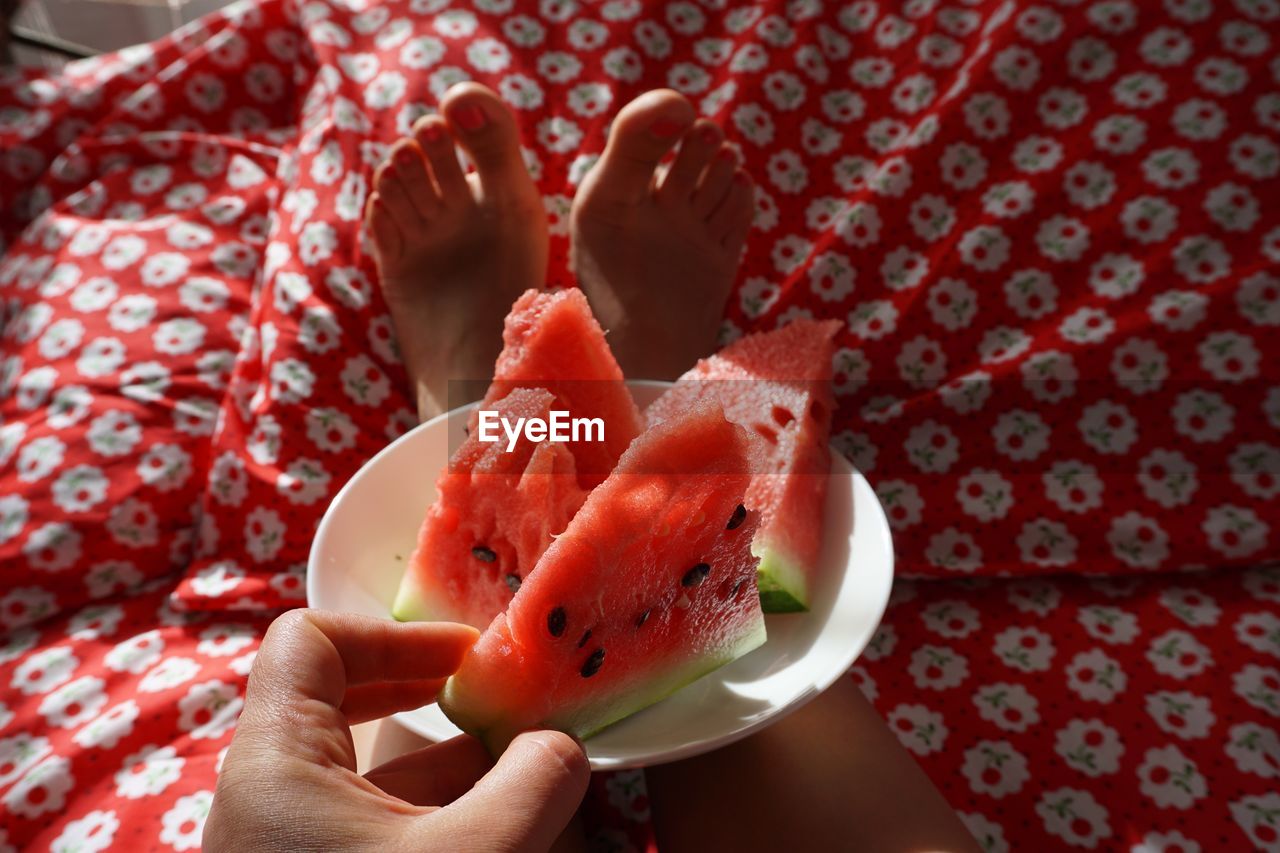 Low section of woman with watermelon slices on bed