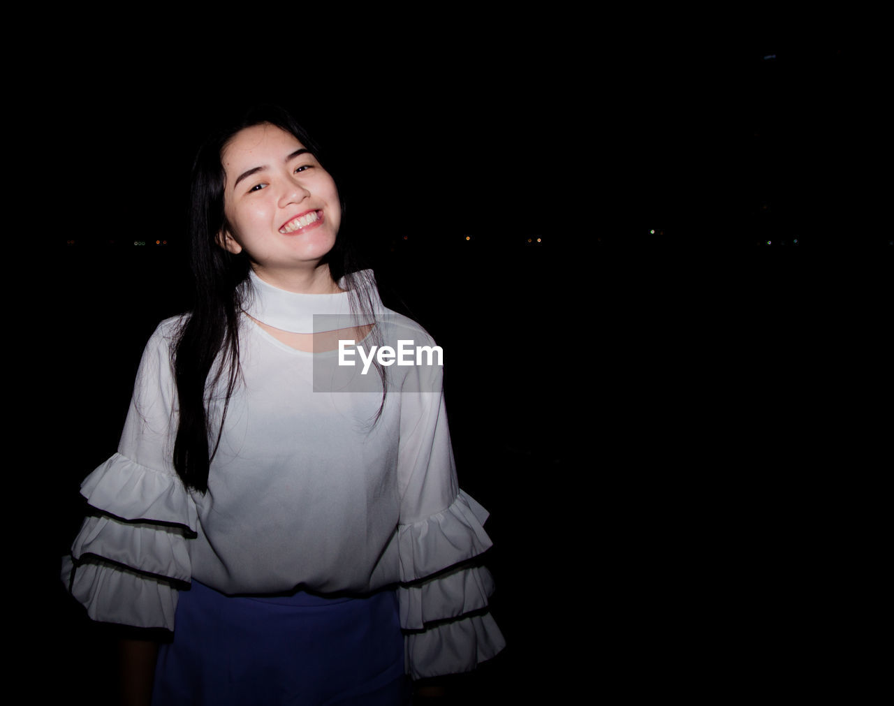 PORTRAIT OF A SMILING GIRL STANDING IN BLACK BACKGROUND