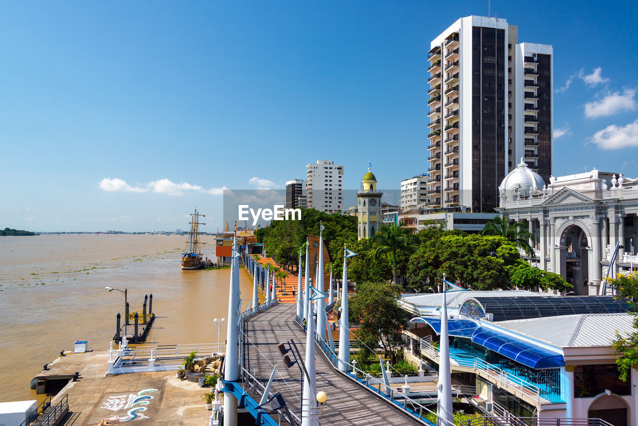 Buildings in city by river against sky