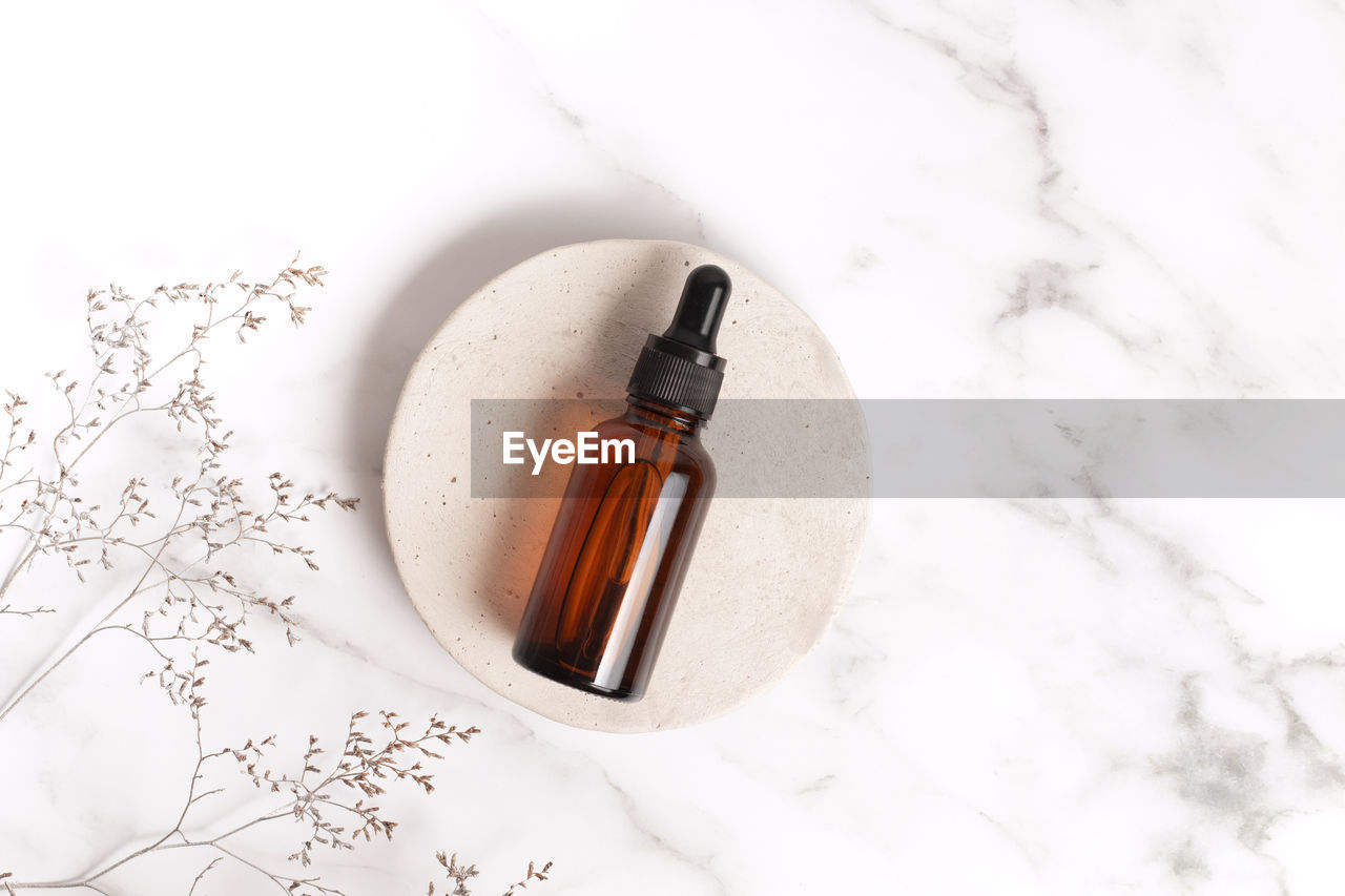 Glass dropper bottle on stone podium on marble background. skincare products