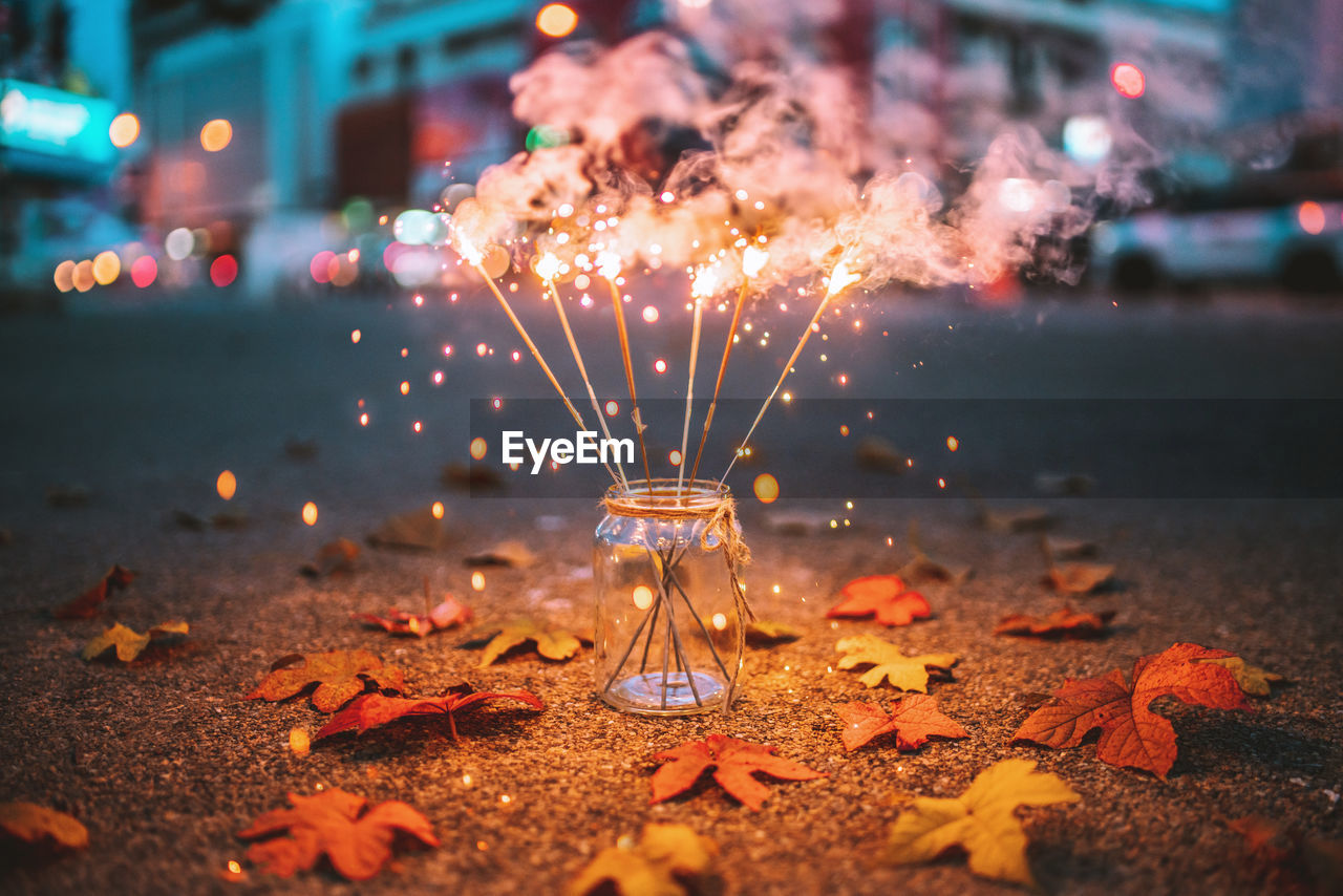 Illuminated sparklers in jar on road at night