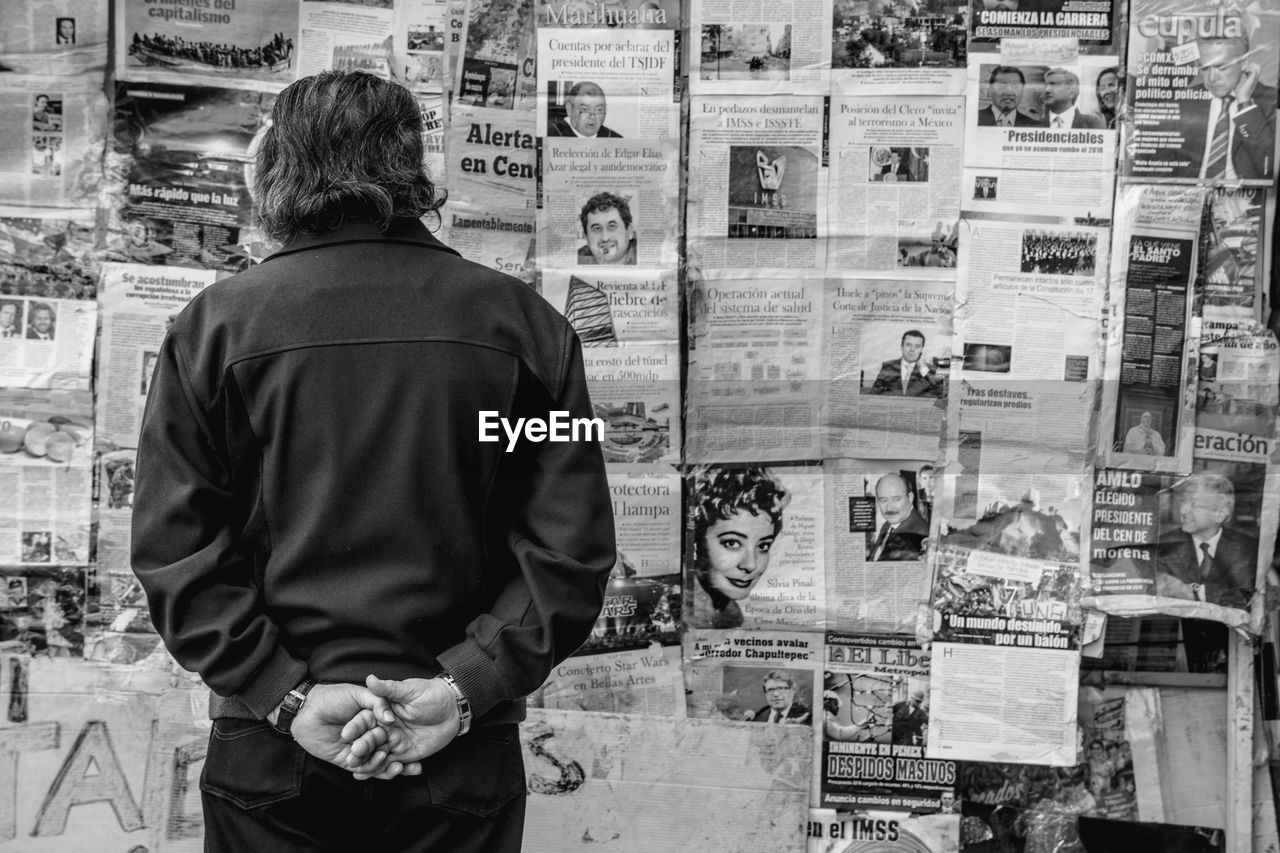 Rear view of man standing against newspapers on wall