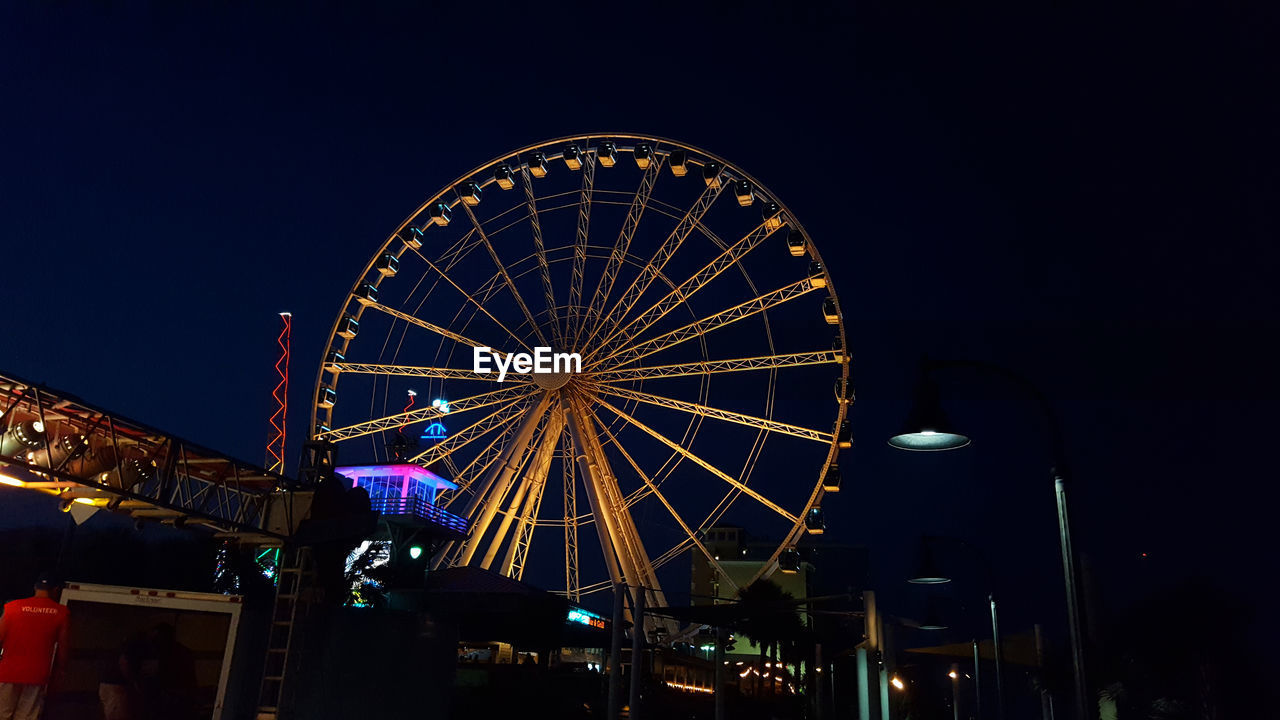 Low angle view of ferris wheel in amusement park at night