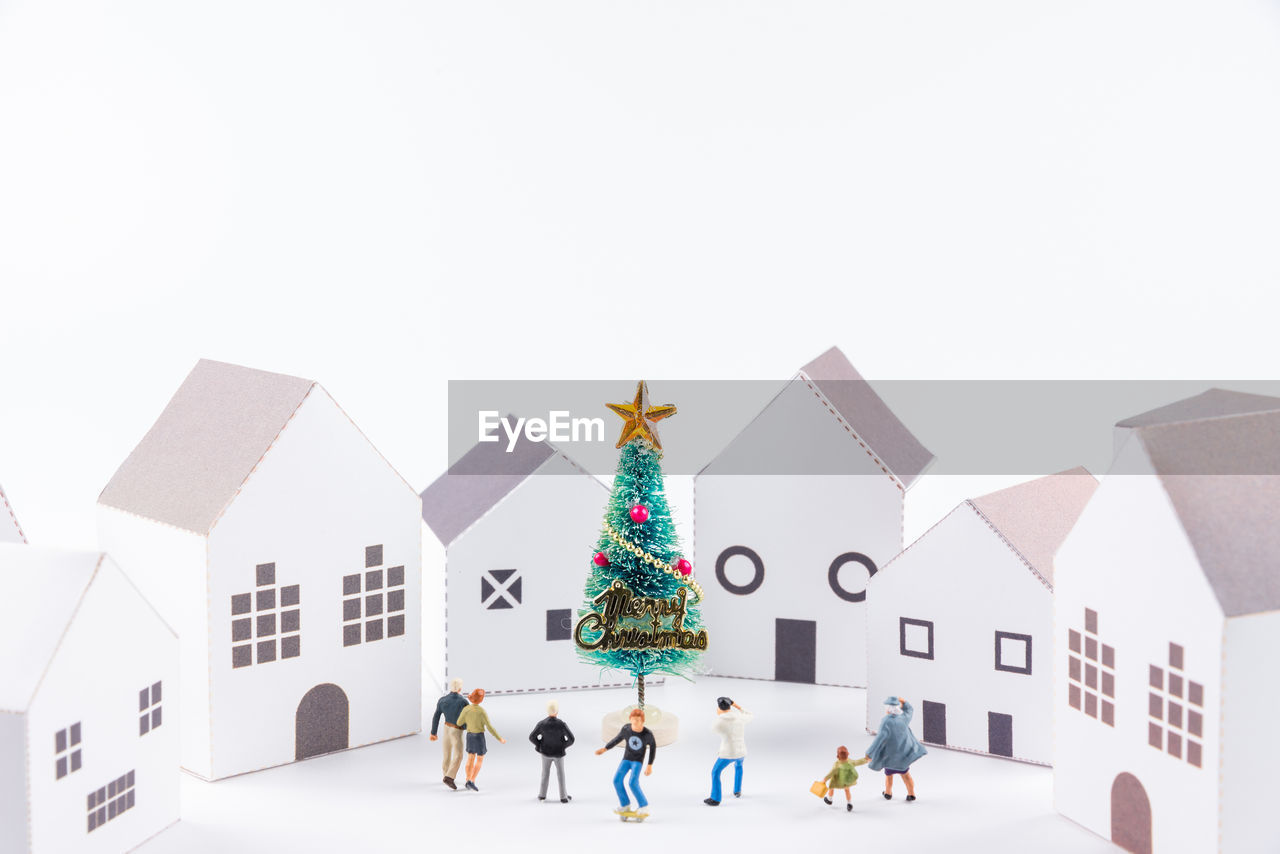 Close-up of figurines with christmas tree and model homes against white background