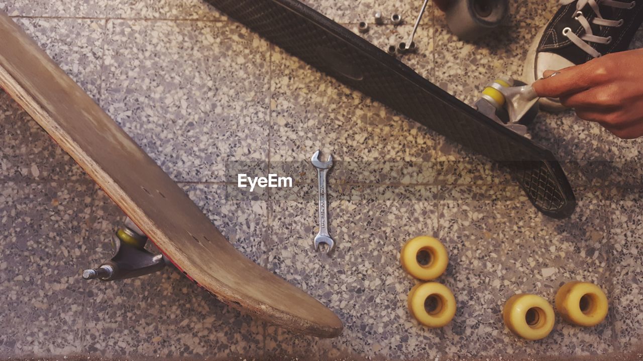 High angle view of man fixing skateboard on tiled floor