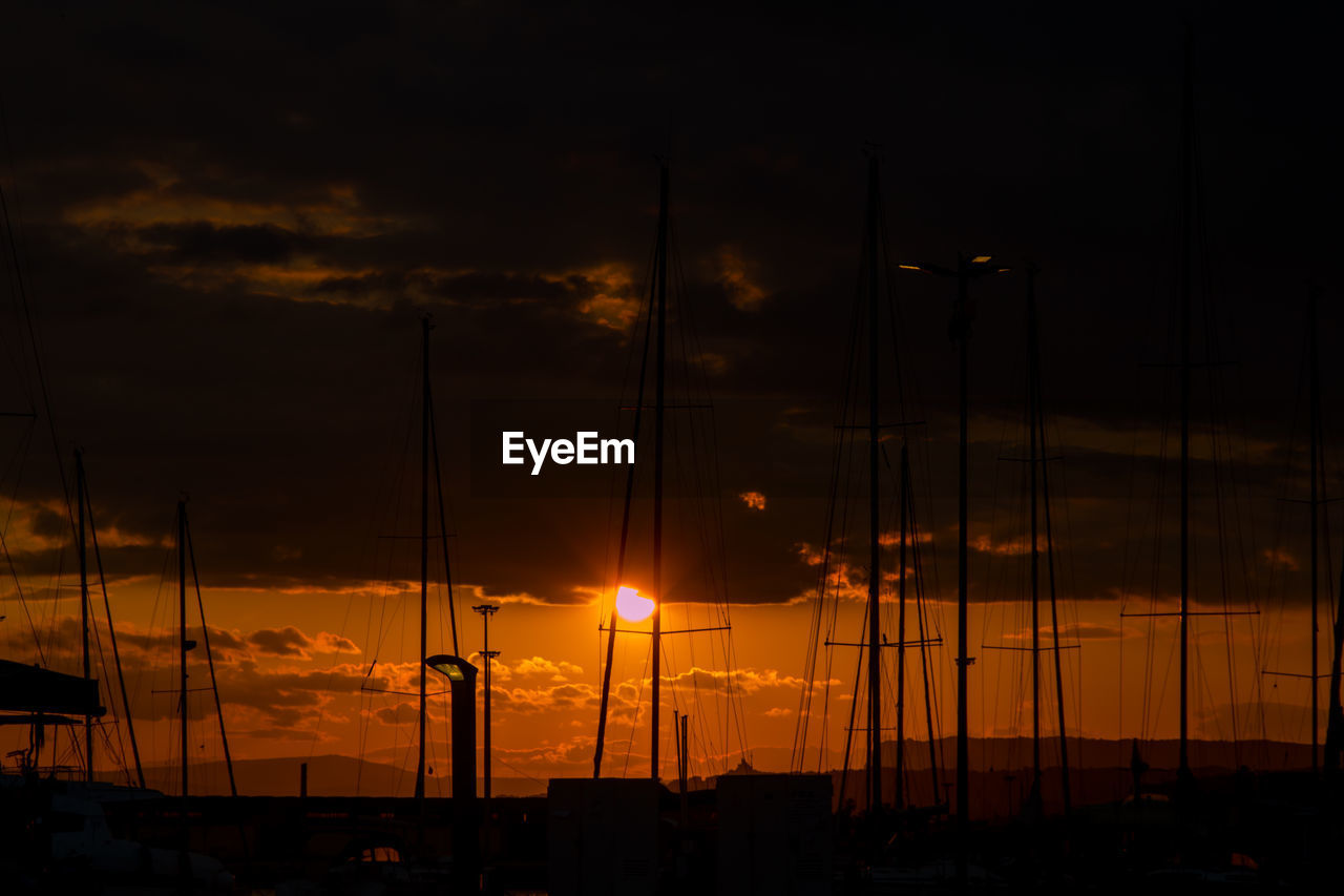 Silhouette sailboats on harbor against orange sky