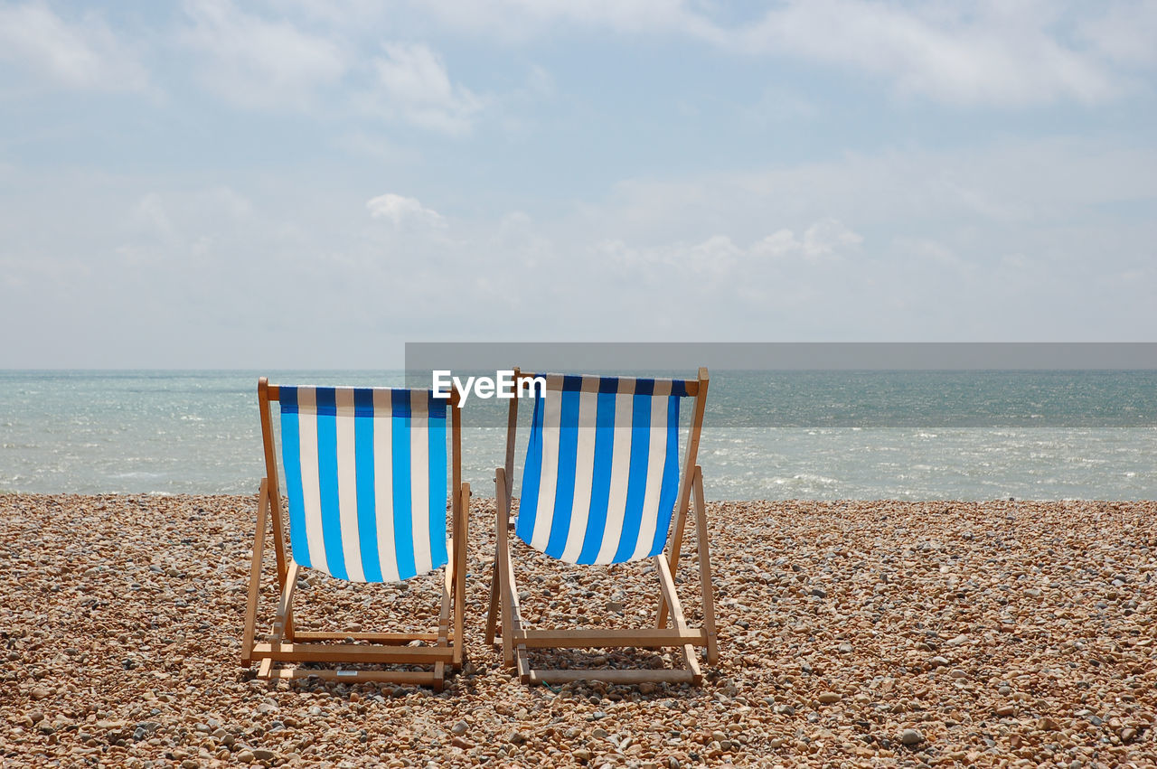 Deck chairs on beach against sky