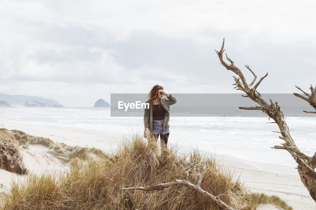 WOMAN STANDING AT BEACH AGAINST SKY