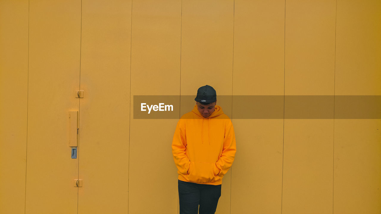 Young man standing against yellow wall