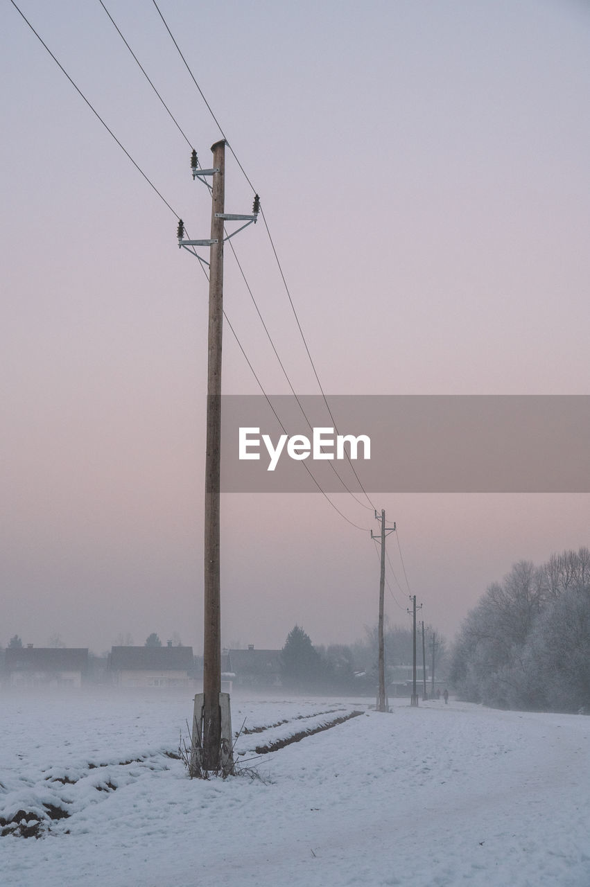 Old wooden electricity pylon in misty winter landscape