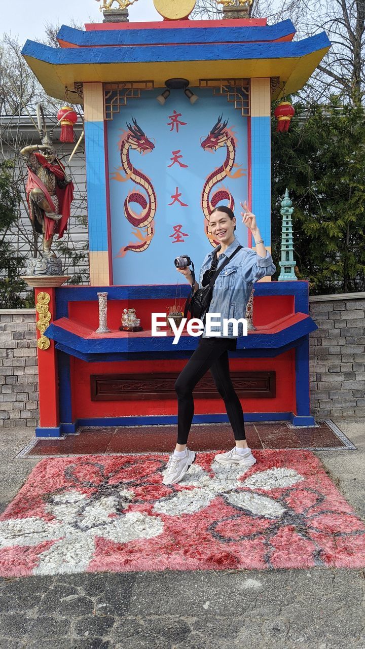 PORTRAIT OF YOUNG WOMAN STANDING AGAINST RED WALL