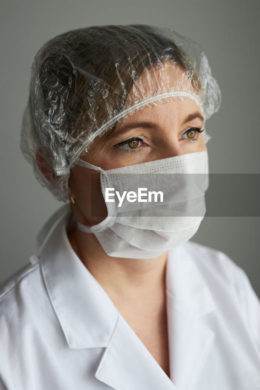 Doctor wearing mask and surgical cap against gray background