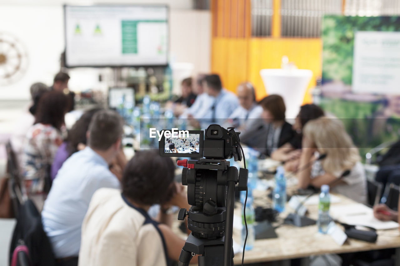 Video camera on tripod filming business meeting in board room during conference