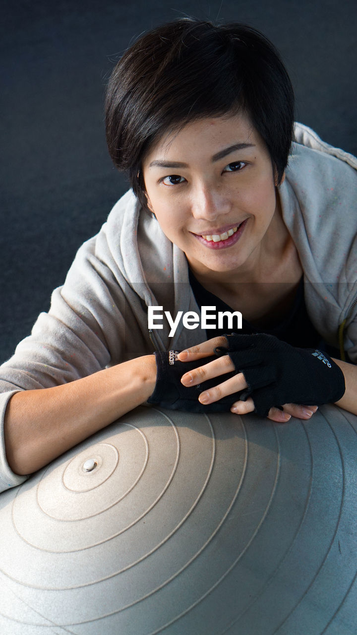 Portrait of smiling woman sitting with fitness ball in gym