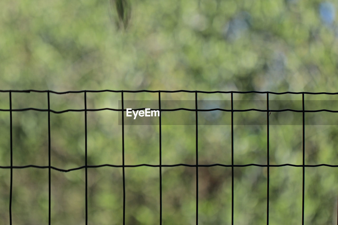 FULL FRAME SHOT OF METAL FENCE AGAINST BLURRED BACKGROUND