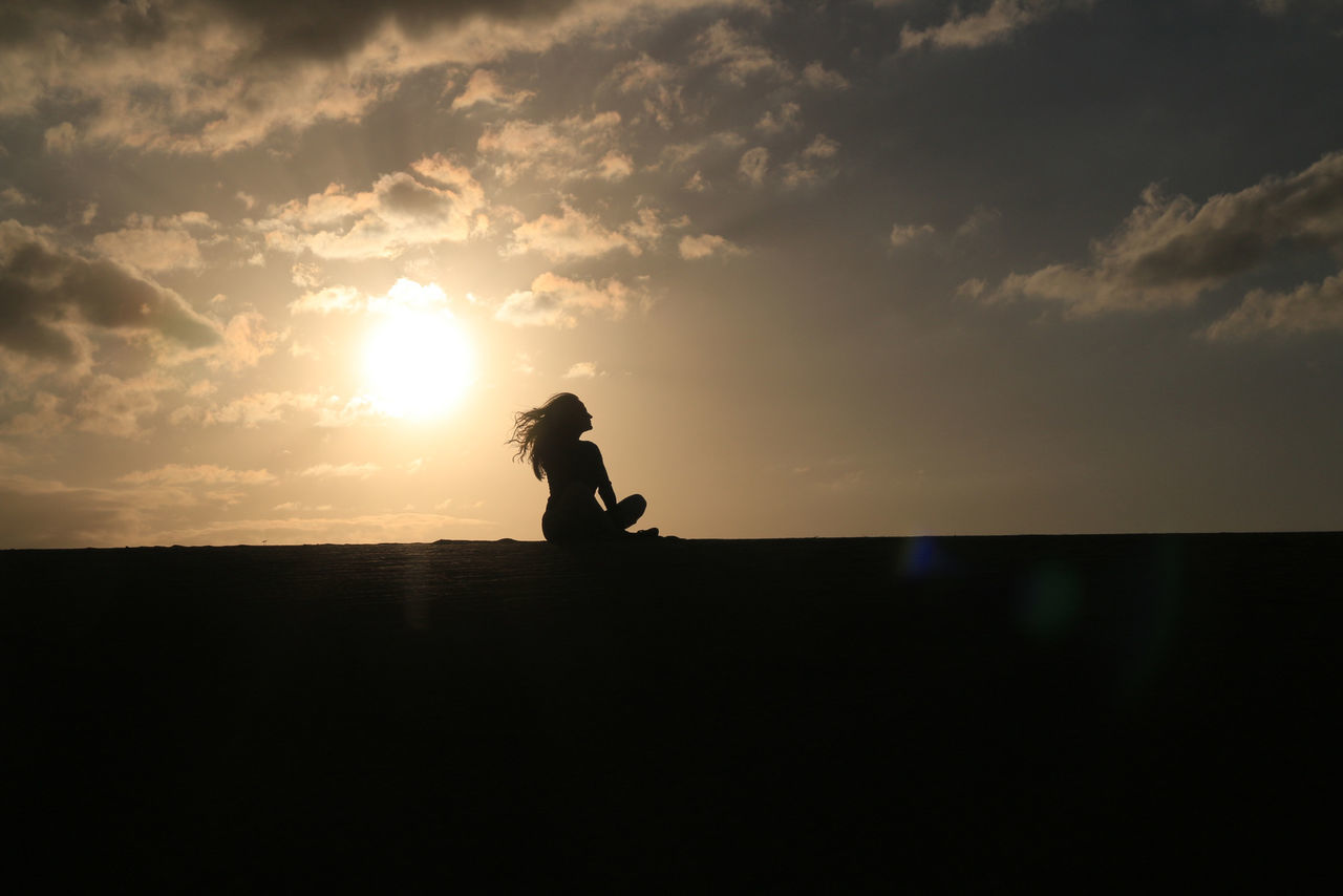Silhouette woman sitting at beach during sunset