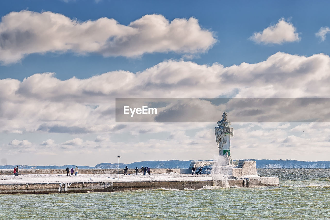 Lighthouse in sea against cloudy sky