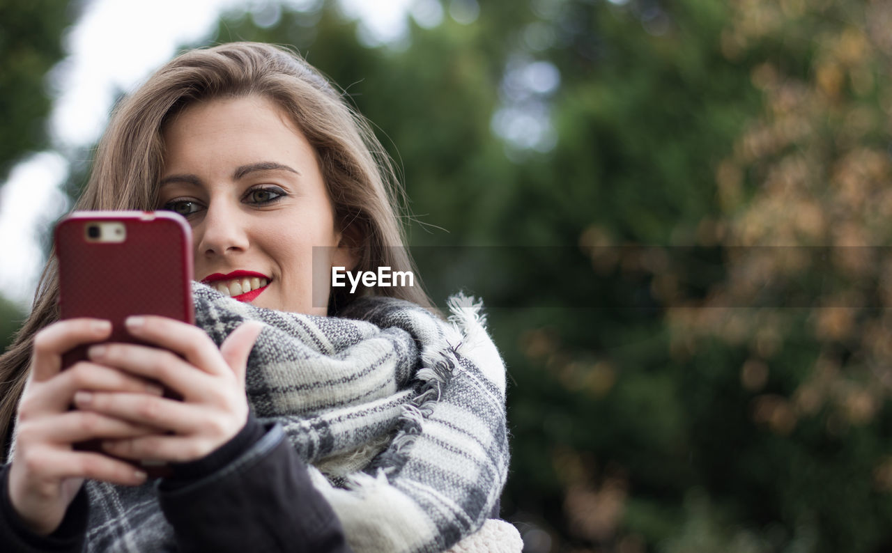 Smiling young woman using smart phone during winter