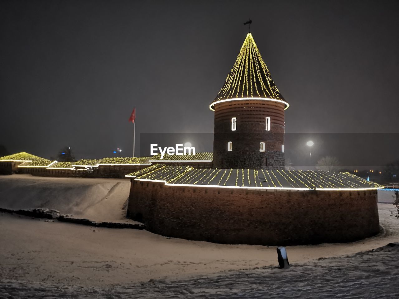 ILLUMINATED LIGHTHOUSE BY BUILDING AGAINST SKY