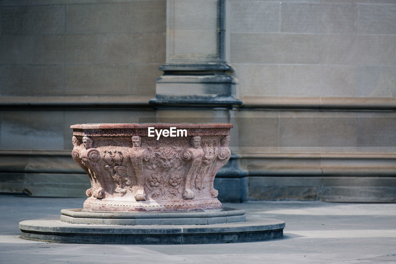 Old carved pedestal on street against wall