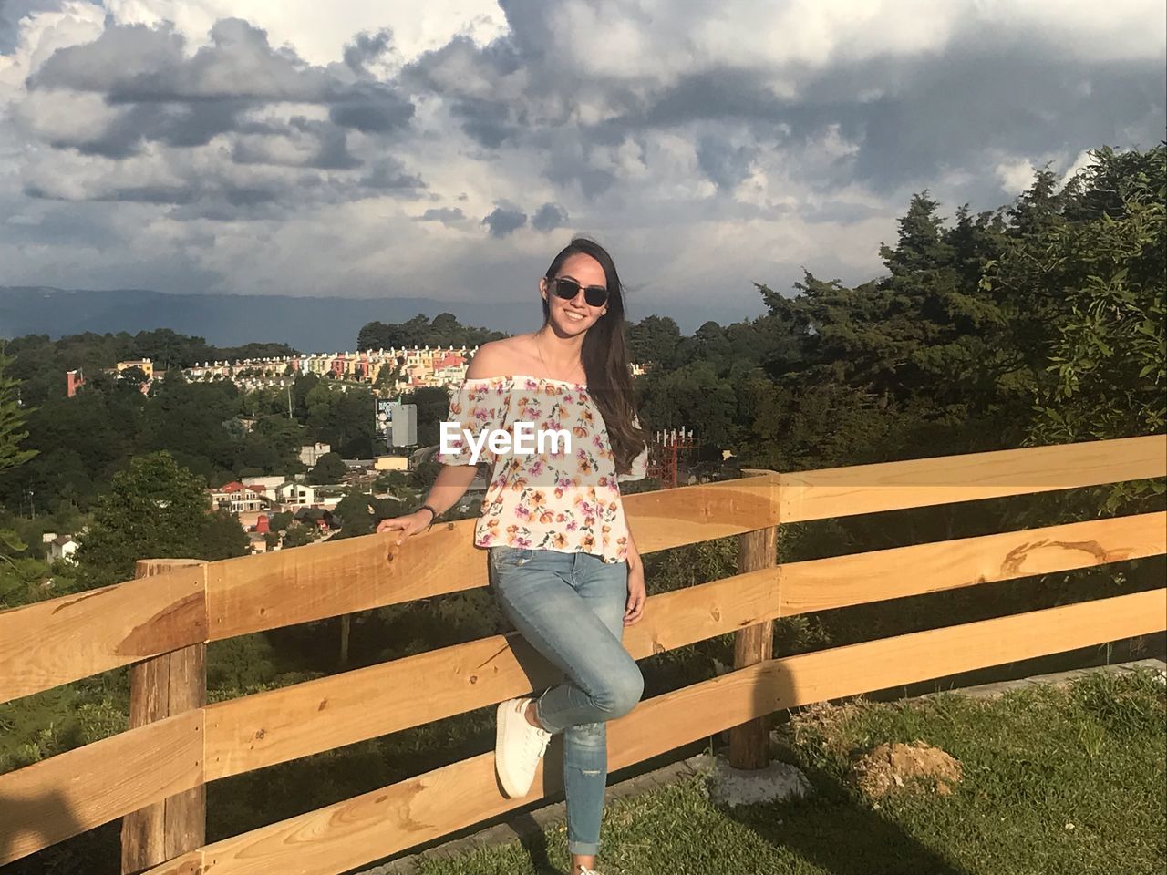 YOUNG WOMAN STANDING BY RAILING AGAINST SKY