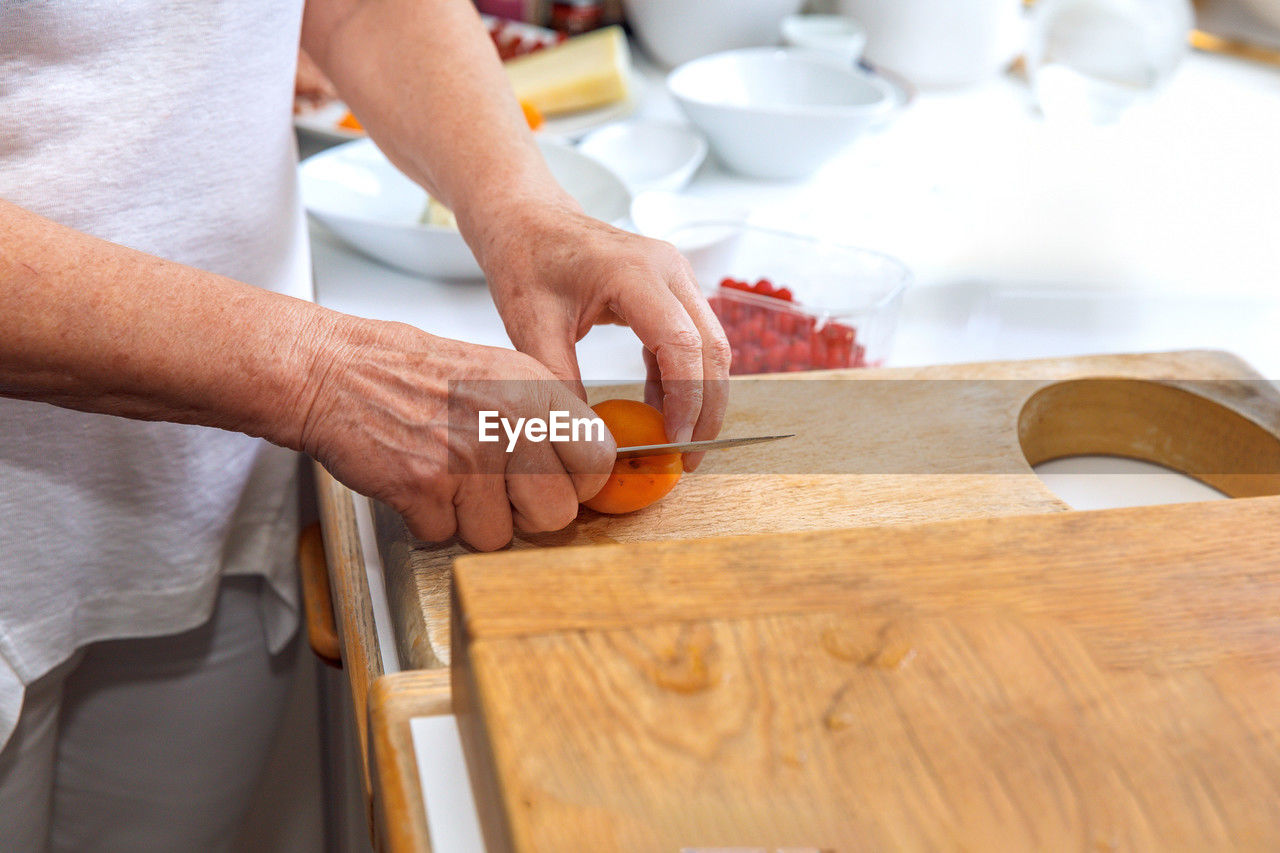 Carefully chopping orange bell pepper on wooden cutting board with hands in the kitchen