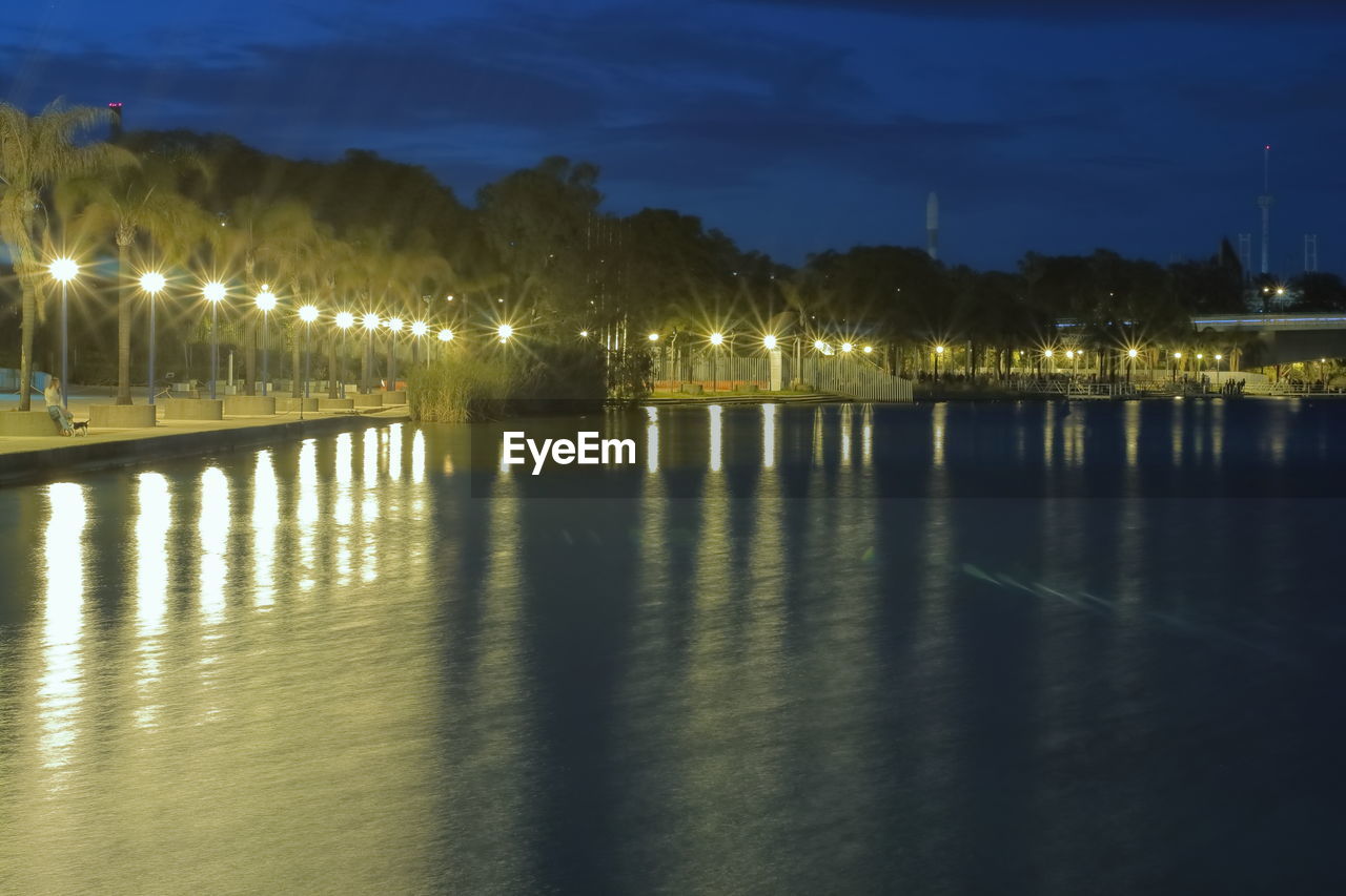 ILLUMINATED STREET LIGHTS BY RIVER AGAINST SKY