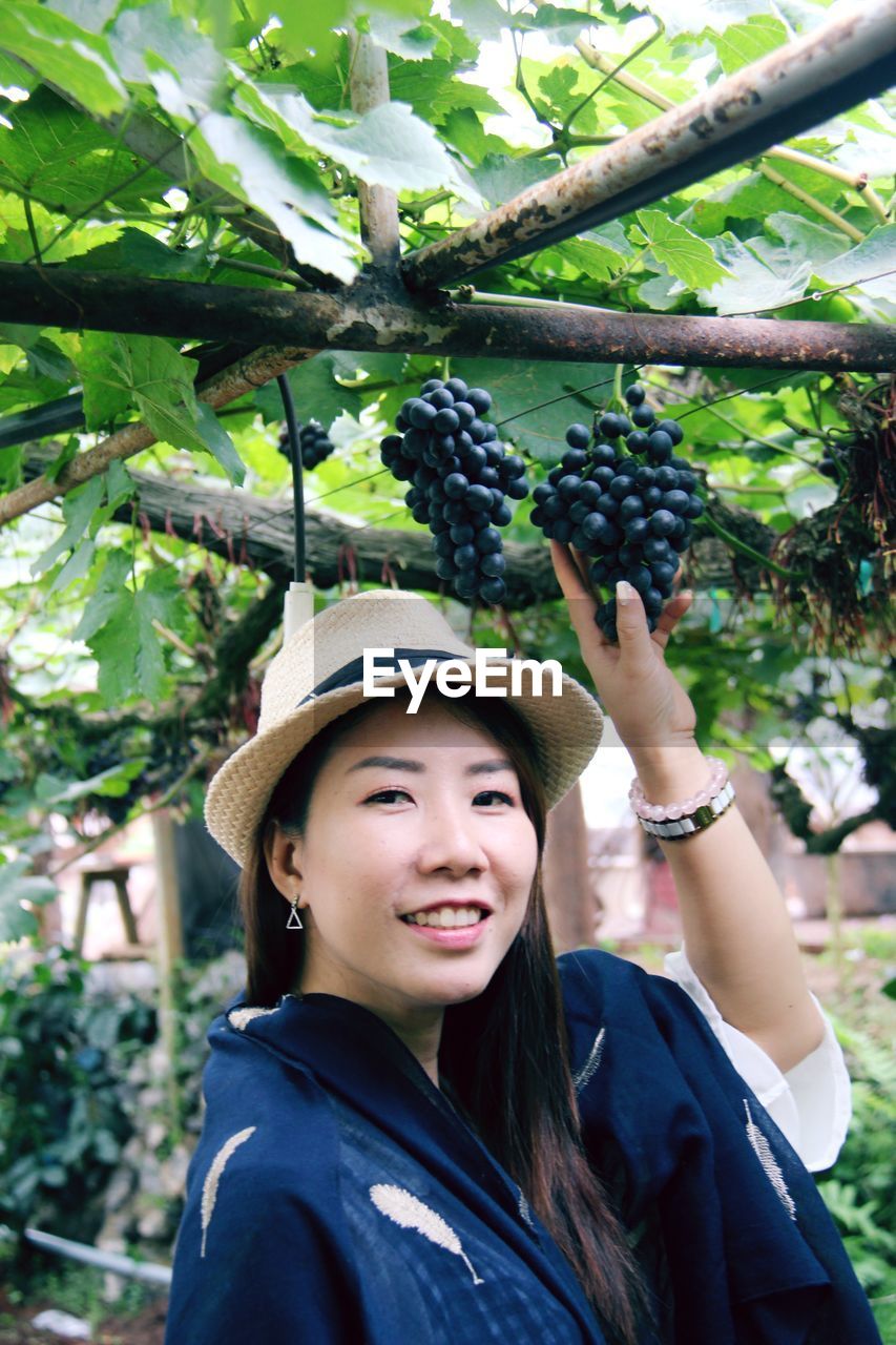 PORTRAIT OF HAPPY YOUNG WOMAN AGAINST TREE