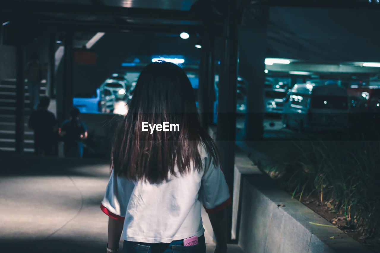 REAR VIEW OF WOMAN STANDING ON FOOTPATH AT NIGHT