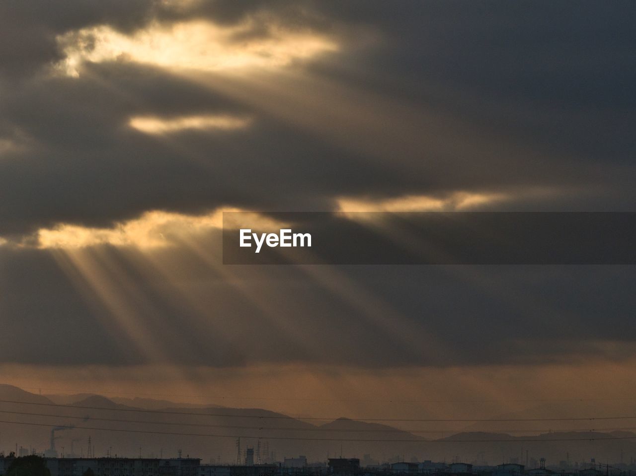 LOW ANGLE VIEW OF SUNLIGHT STREAMING THROUGH CLOUDS OVER LANDSCAPE