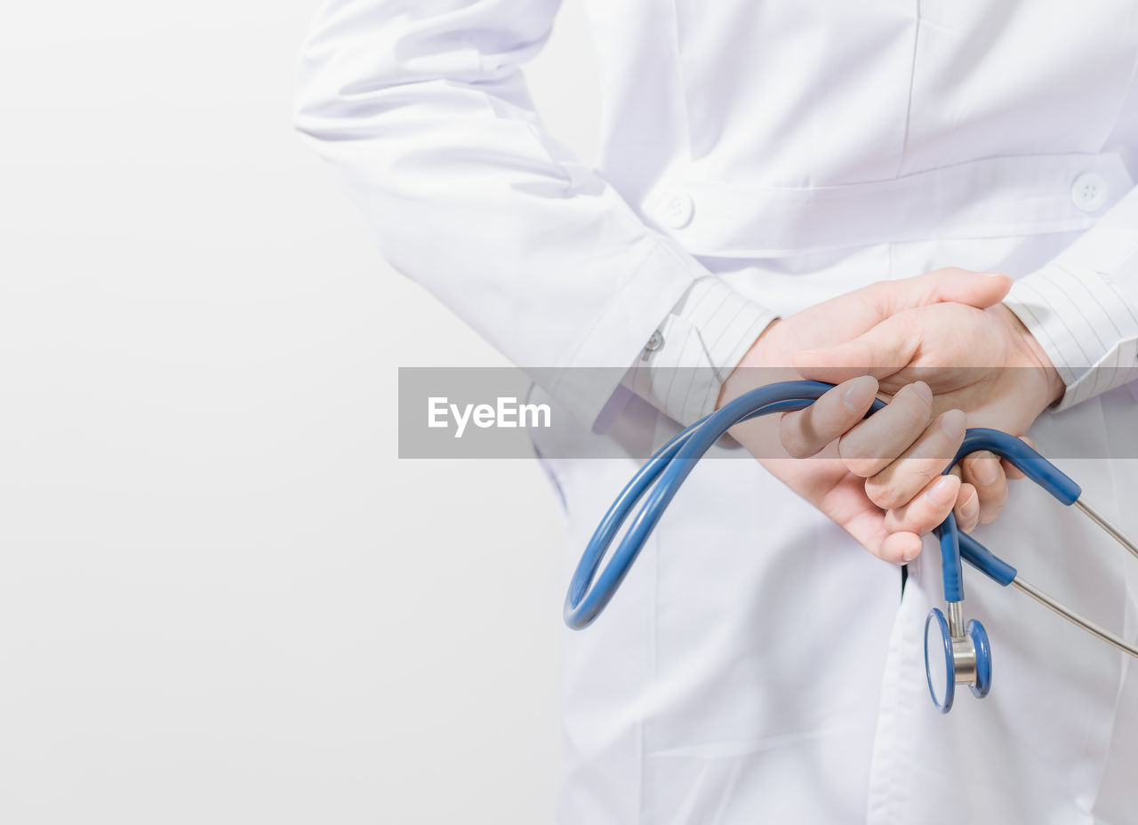 Midsection of doctor holding stethoscope standing against white background