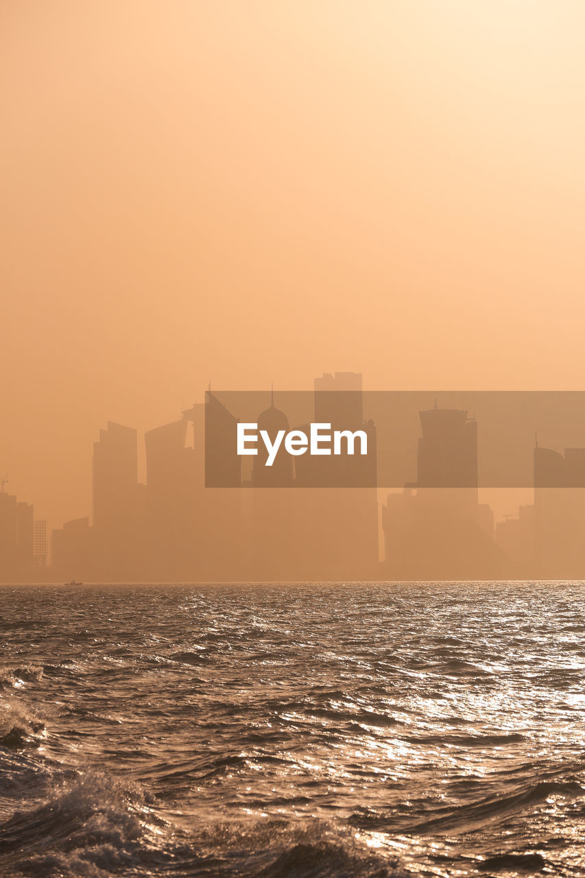 Sea by buildings against sky during sunset