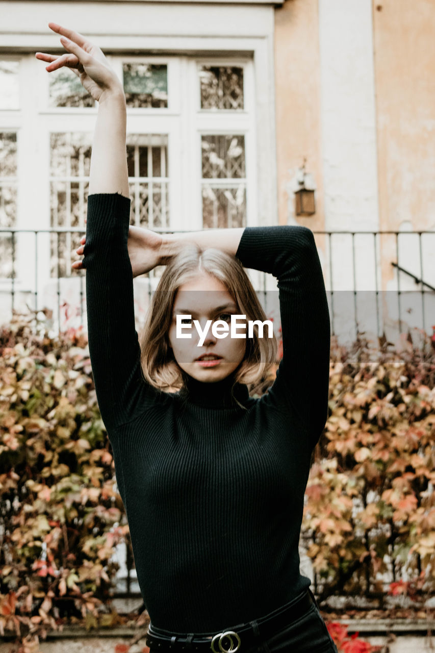 PORTRAIT OF YOUNG WOMAN WITH ARMS RAISED STANDING IN FRONT OF FACE